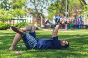 Dad laying in grass holding up toddler